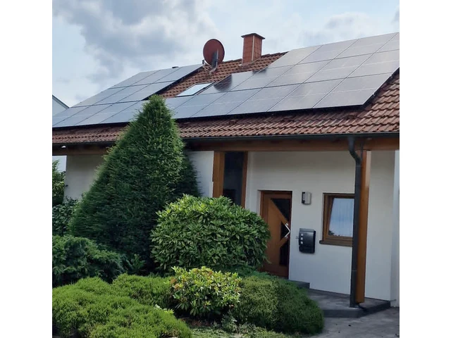 Freistehendes Einfamilienhaus mit rotem Ziegeldach, großflächig mit schwarzen Solarmodulen belegt