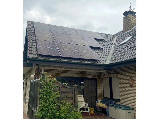 Einfamilienhaus mit dunklem Ziegeldach und Klinkerfassade, schwarze Solarmodule über der Terrasse