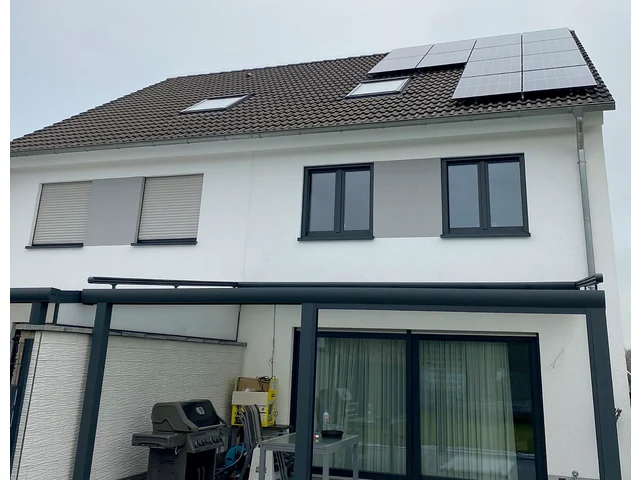 Weiße Doppelhaushälfte mit Solarmodulen auf dem dunklen Ziegeldach, davor eine überdachte Terrasse