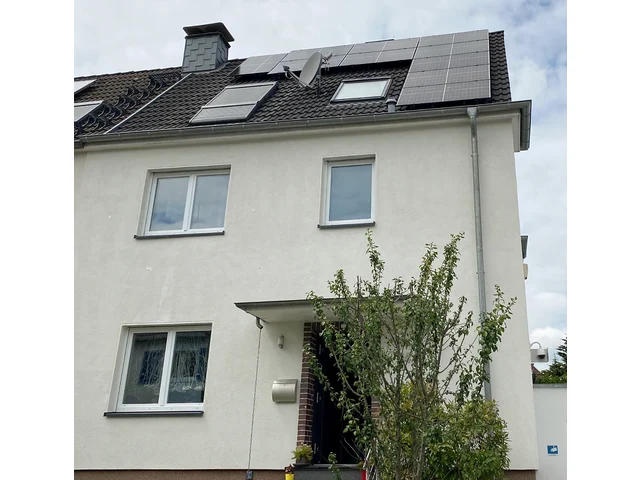 Helle Doppelhaushälfte mit schwarzen Solarmodulen zwischen Dachfenstern auf dunklem Ziegeldach