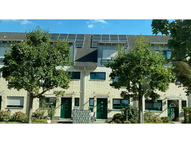 Reihenhauszeile mit heller Klinkerfassade und grünen Haustüren, Solarmodule auf zwei Dächern
