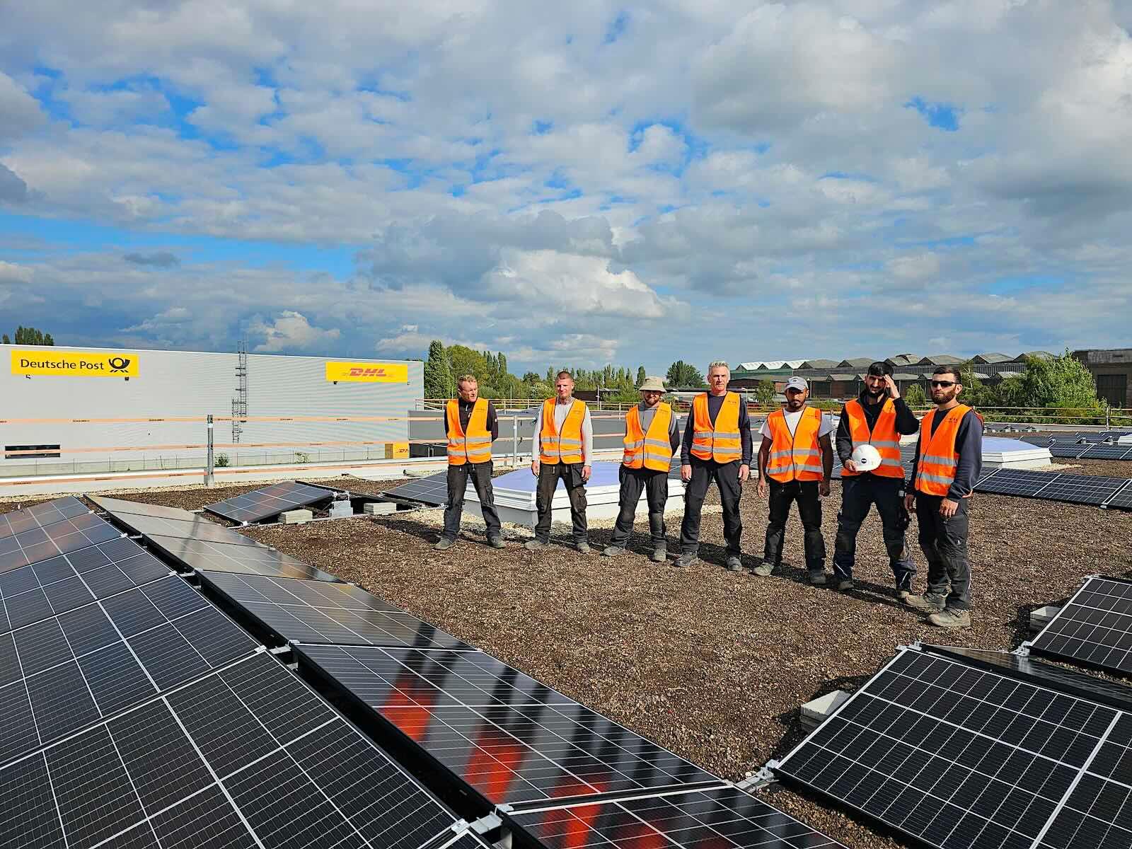 Historische INTRA-Projektaufnahme: Photovoltaikmodule, damalige Mitarbeitende und DHL-Gebäude im Hintergrund